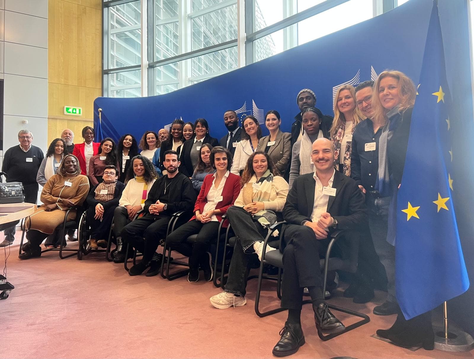 Fotografia de grupo durante uma visita institucional na Comissão Europeia, com o painel da Comissão e a bandeira europeia ao fundo.